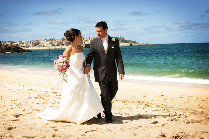 photograph by Shah Photography of bride and groom walking along Porthminster beach at St Ives in Cornwall