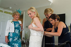 bride helped into her wedding dress by her bridesmaid