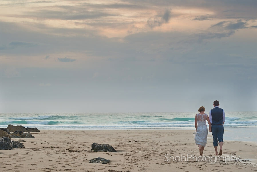 The bride and groom walk towards the sea under a dramatic sky on this beach at St Agnes in Cornwall
