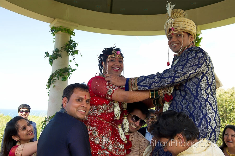 Hindu wedding ceremony photograph which feathers the smiling bride and groom being lifted by laughing guests
