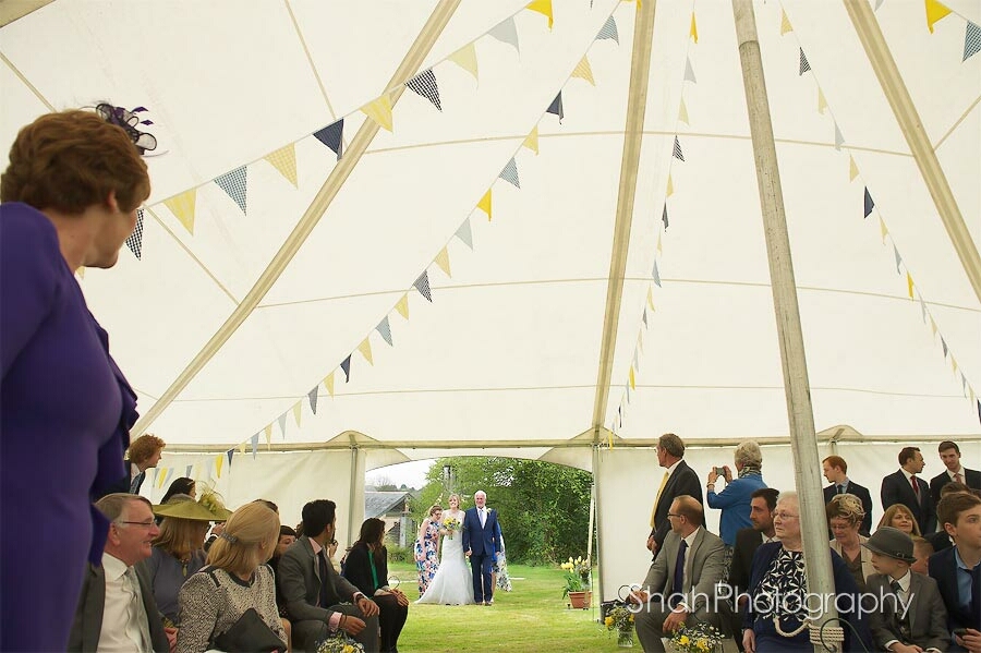 The bride and her father make their way to the wedding marquee watched by the wedding guests 