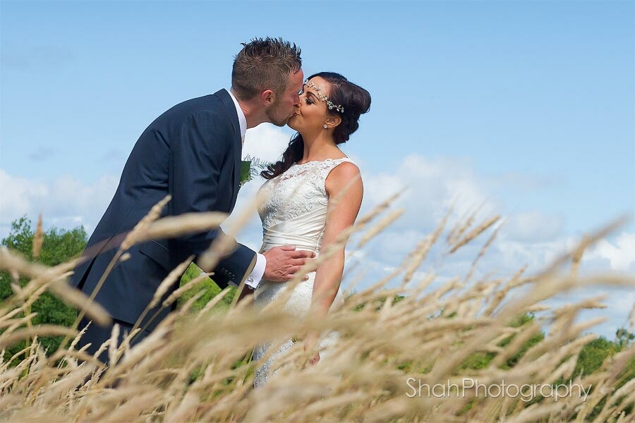 The bride and groom kissing with a background of blue sky and foreground of grasses blowing in the breeze