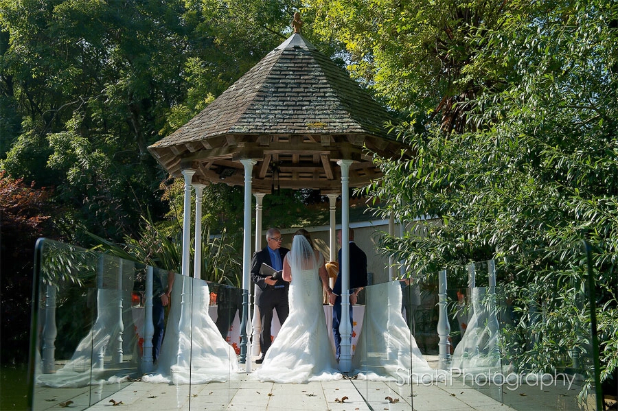 The bride and groom photographed from behind during their wedding ceremony with reflections of the dress either side