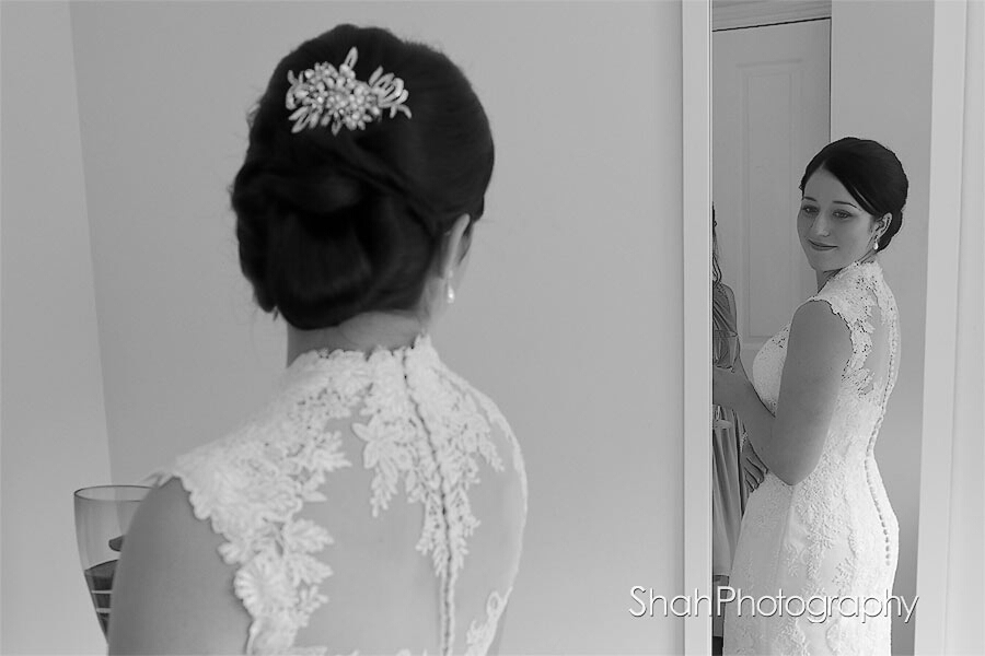 Bride looking at her reflection in a mirror sees her wedding dress whilst holding a glass of bubbly