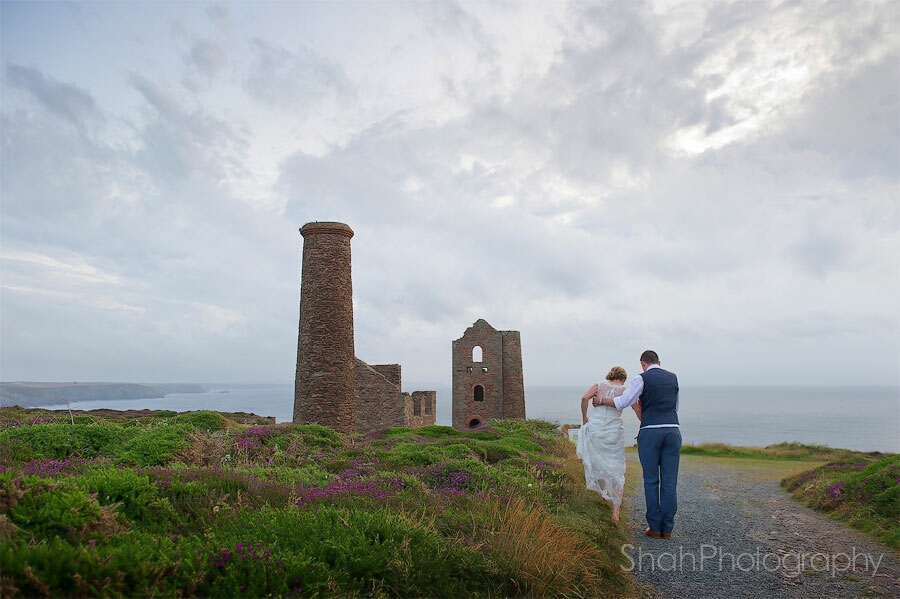 Sea view, heather, a Cornish tin mine make a stunning backdrop to the bride and groom walking away from the camera