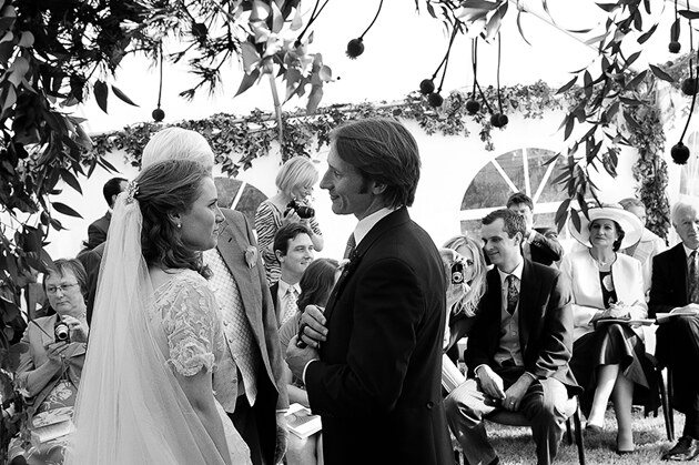 bride and groom photographed during the signing of the marriage register watched by their guests